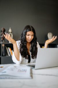 A frustrated businesswoman sits at her office desk, puzzled over her laptop.