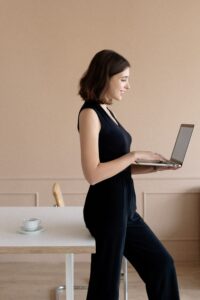 Side view of a smiling woman using a laptop in an indoor setting, representing modern work culture.
